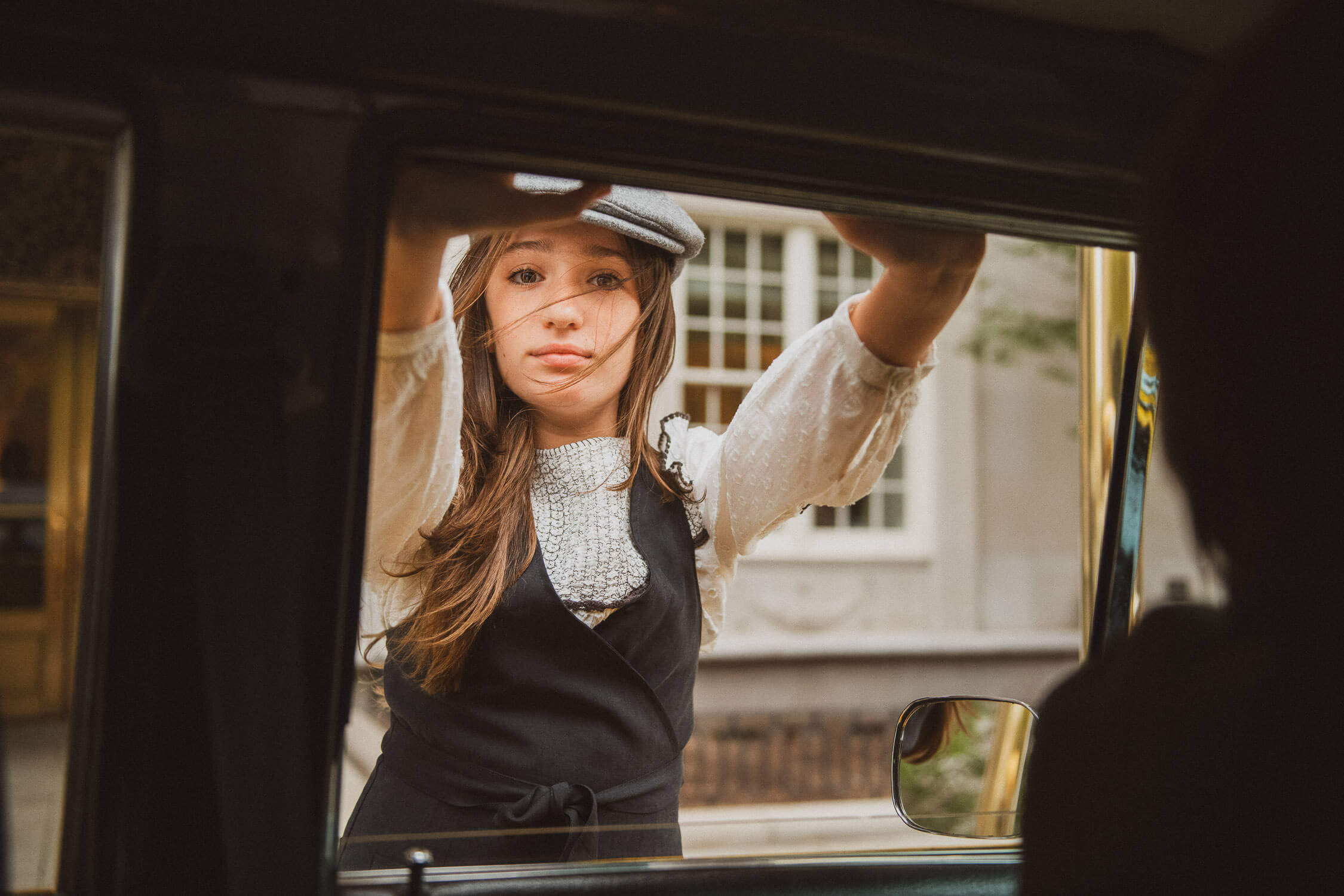 girl looking through a car window with a curious expression, wearing a newsboy cap