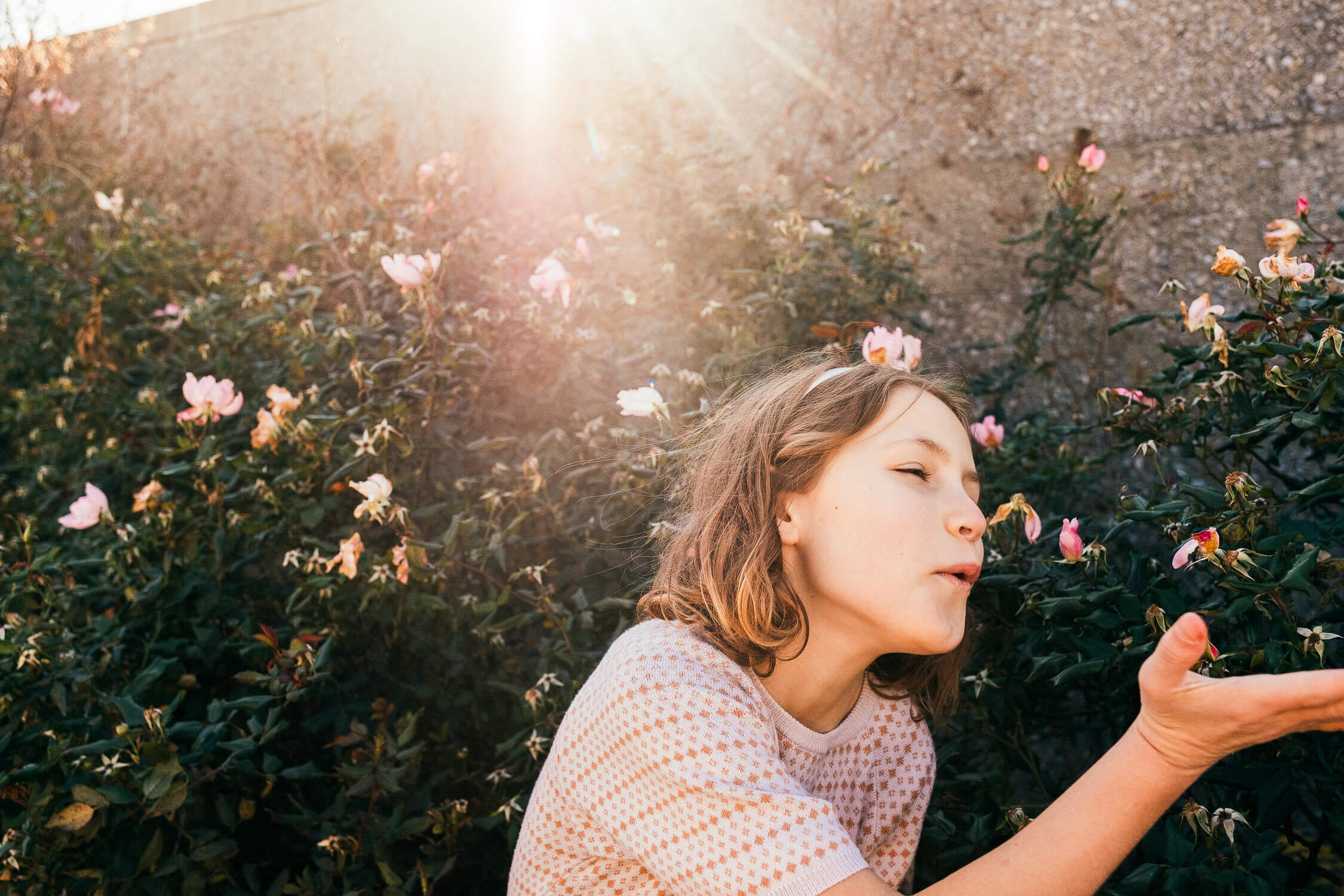 girl examining flowers in a sunlit garden, delicate moment with sun rays in the background