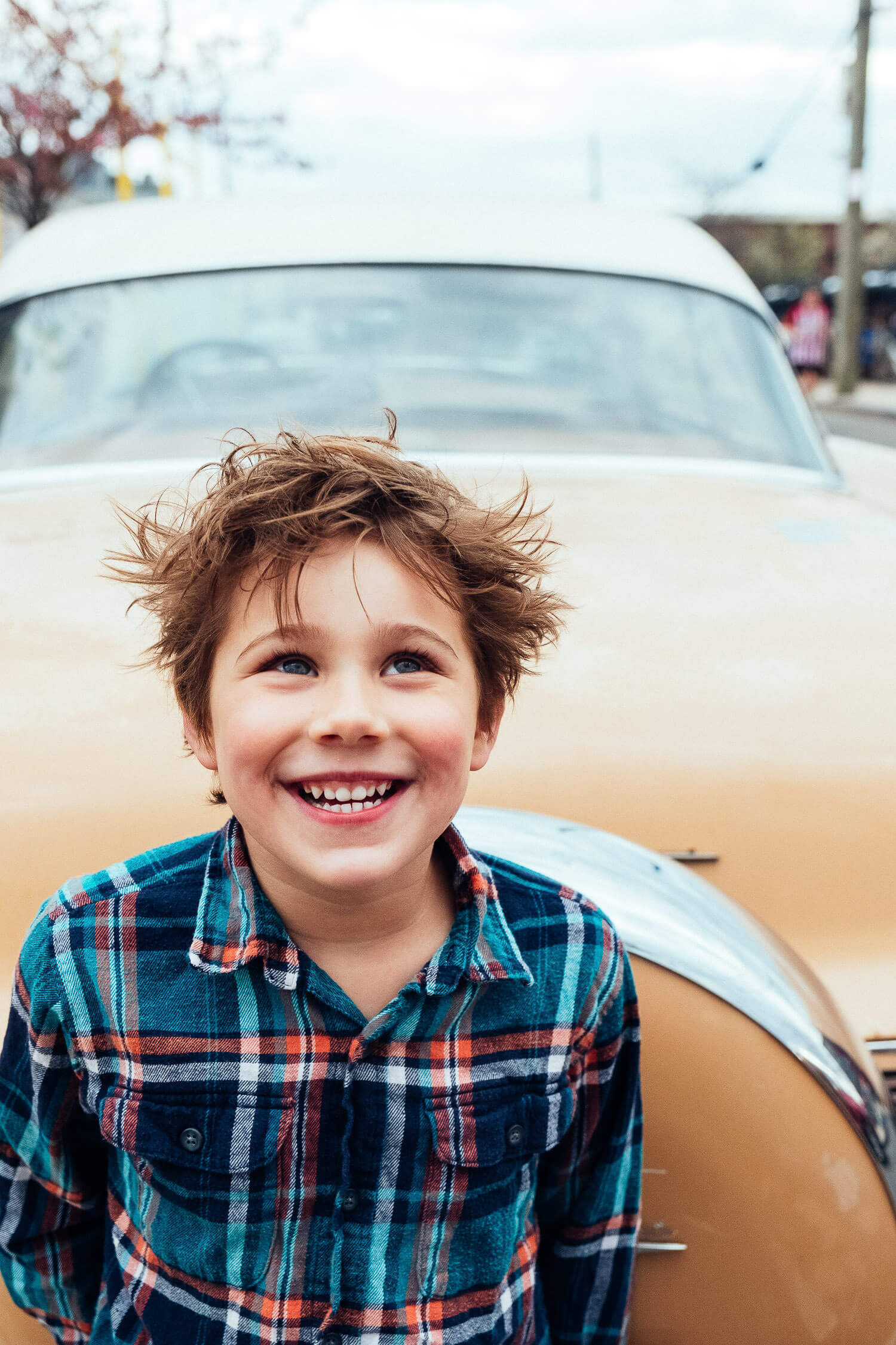 young boy smiling in front of a vintage car, capturing joyful childhood energy