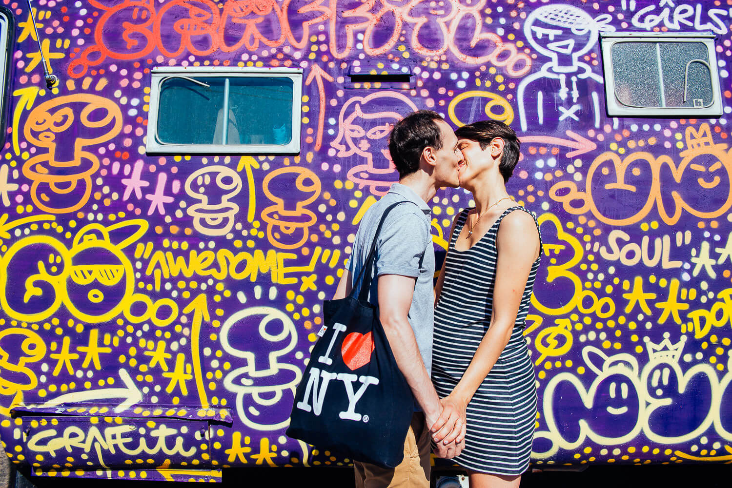 Couple sharing a kiss in front of a vibrant, graffiti-covered wall in NYC, embodying a playful and urban lifestyle photography session.