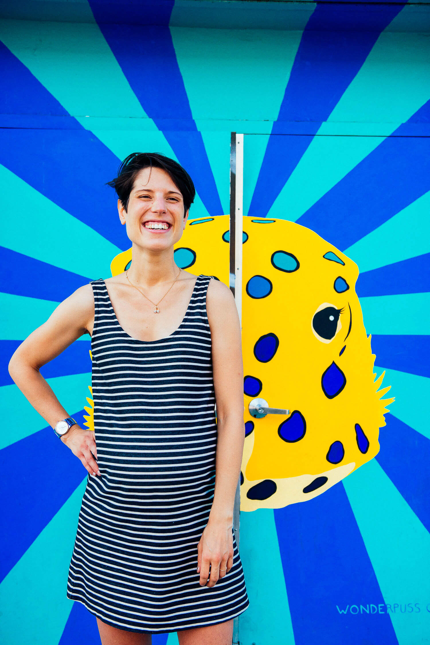 Pregnant woman in a striped dress laughing in front of a bright mural.