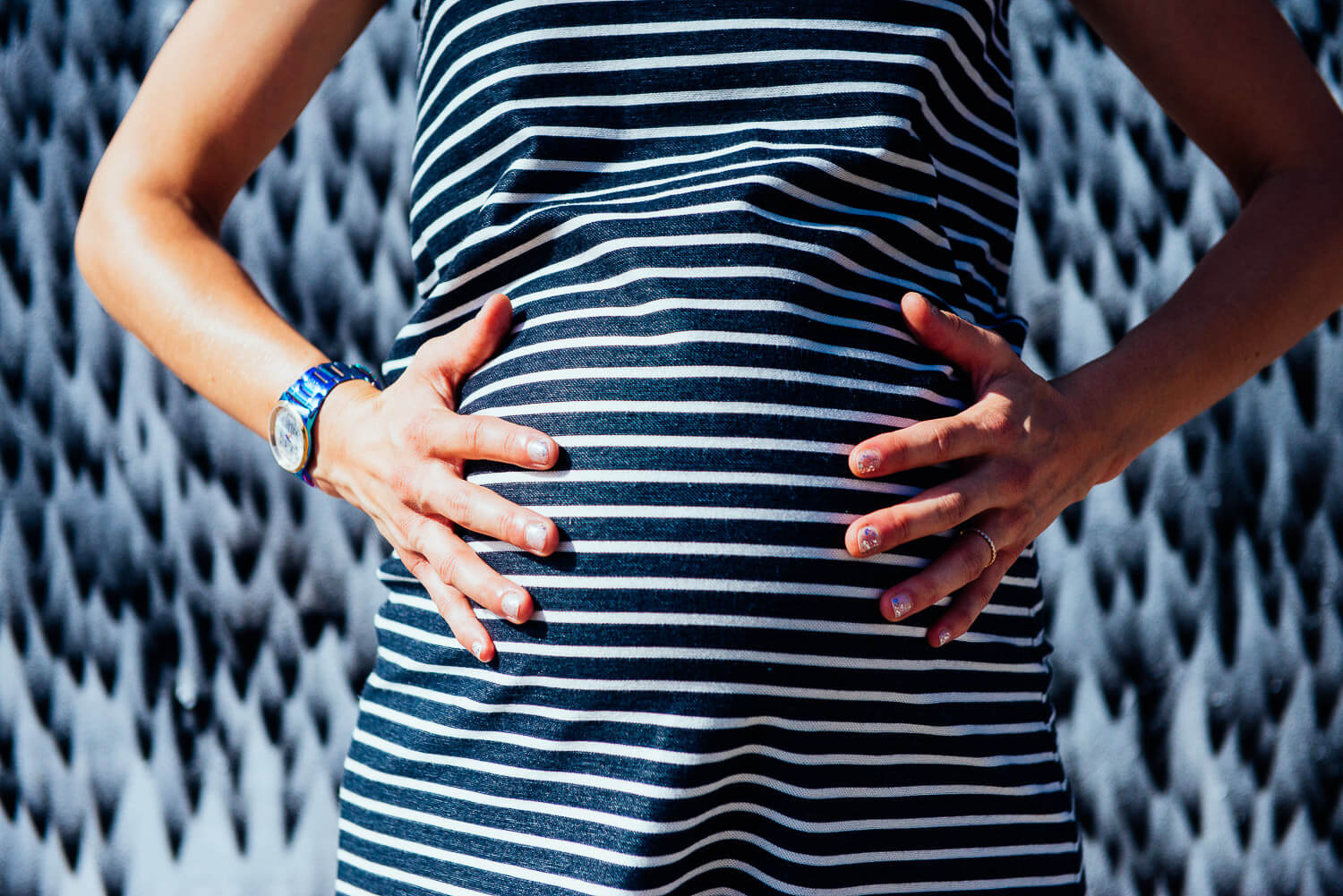 Maternity photoshoot in Brooklyn NYC of pregnant mother holding her stomach wearing a striped tshirt.