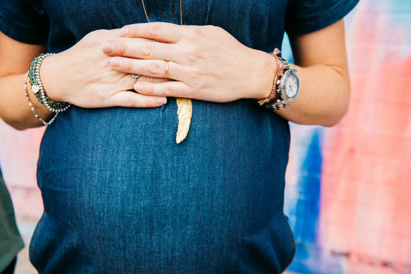 Close-up of hands resting on a pregnant belly with a feather necklace.