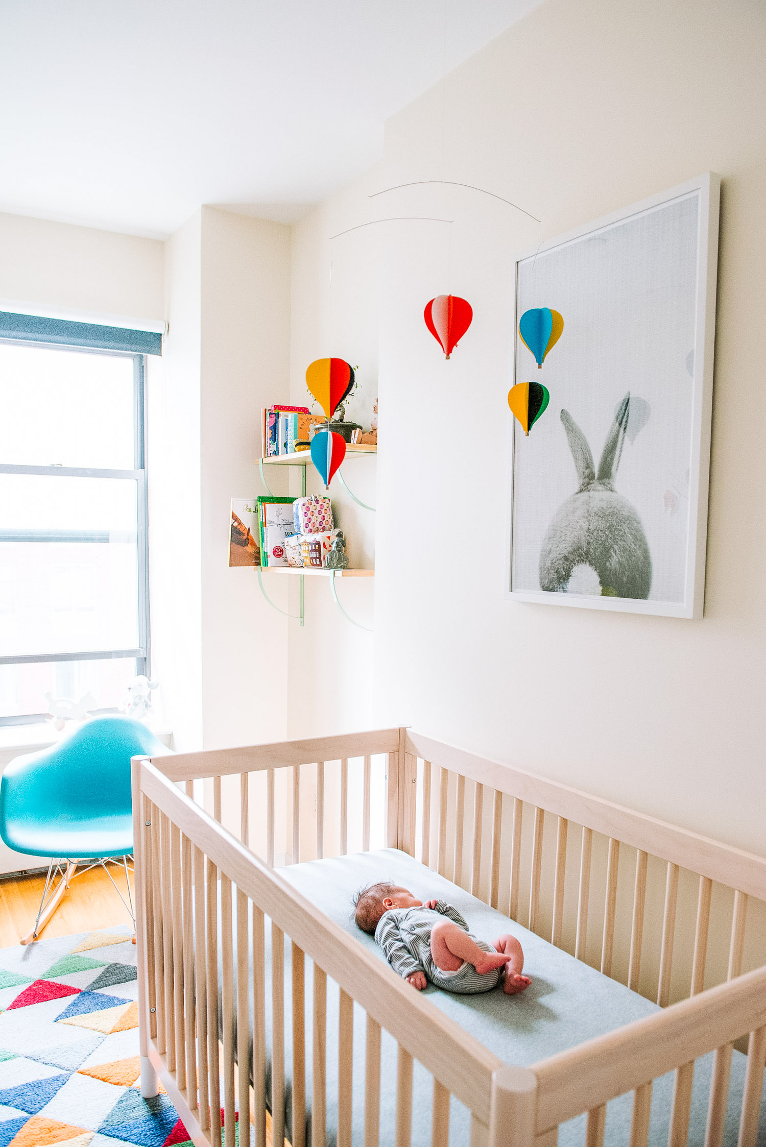 New mom standing beside crib in small NYC apartment nursery during newborn photography session