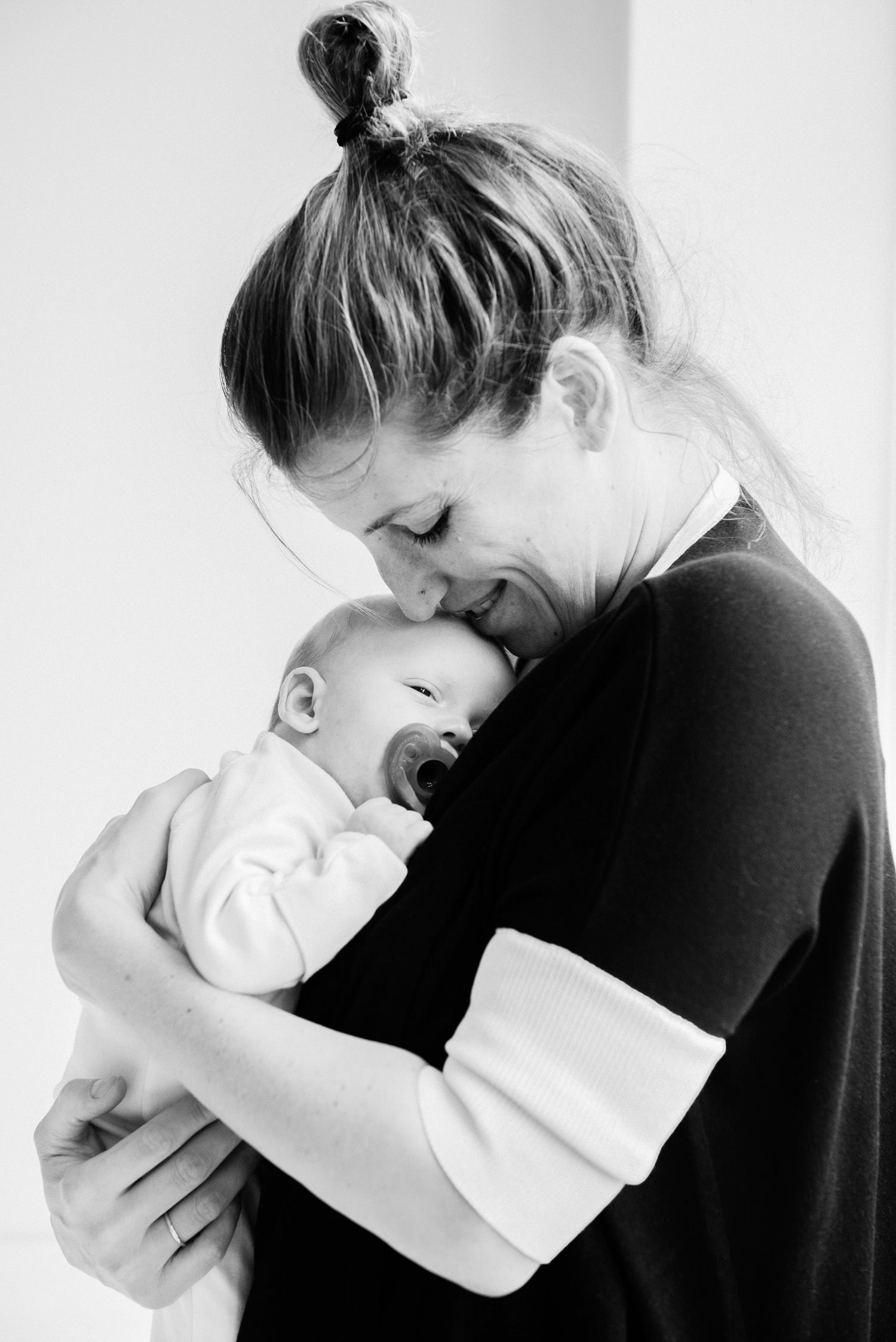 Traditional black and white newborn photo of smiling mother holding baby in Brooklyn apartment