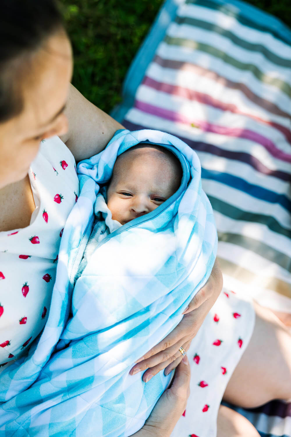 Mother gently holding newborn baby wrapped in blue blanket during outdoor session in natural light